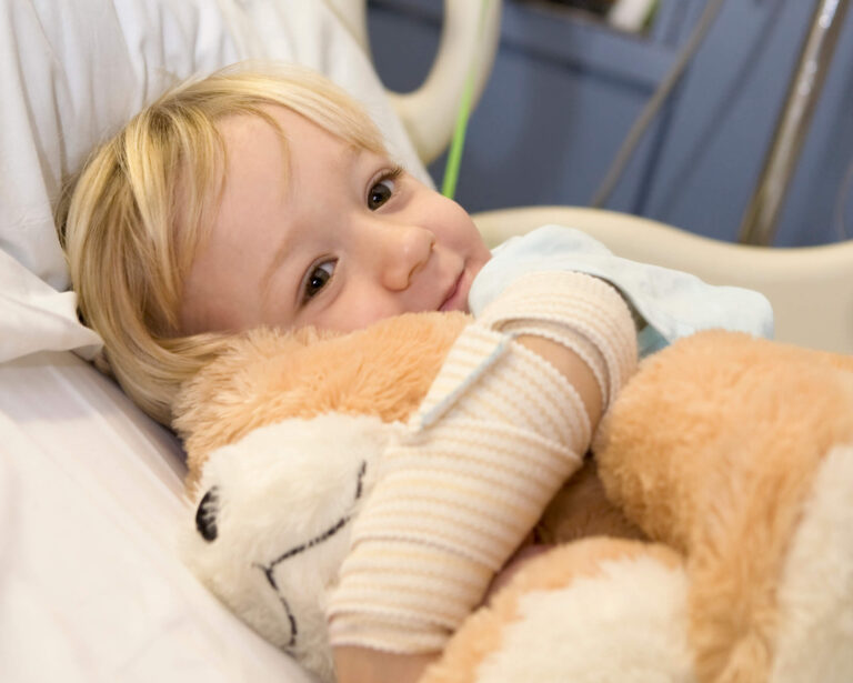 Little girl holding teddy bear with a cast on her arm.
