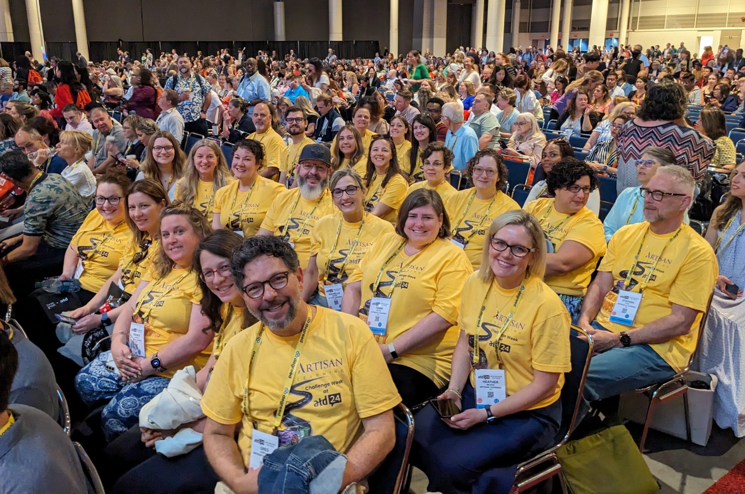 Artisan Learning team members in matching yellow shirts are seated together at a conference.