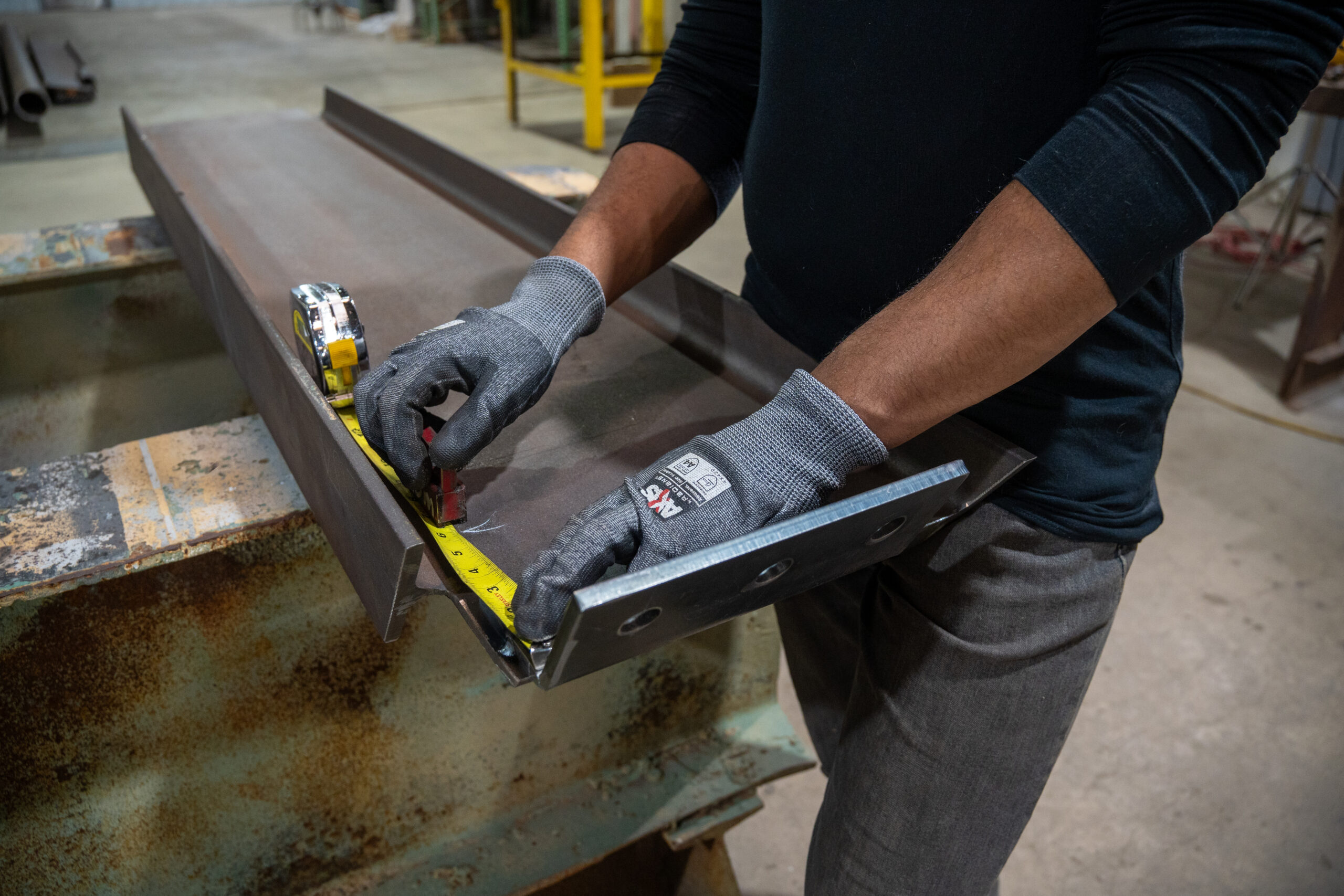 A steel worker uses a tape measure to mark a piece of steel.