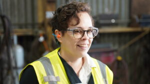 Artisan lead instructional designer, Jill Marshall, smilles while working onsite at a steel fabrication shop.