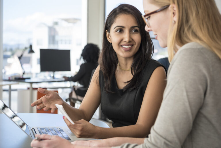 Mid adult businesswoman listening to female colleague in office - stock photo