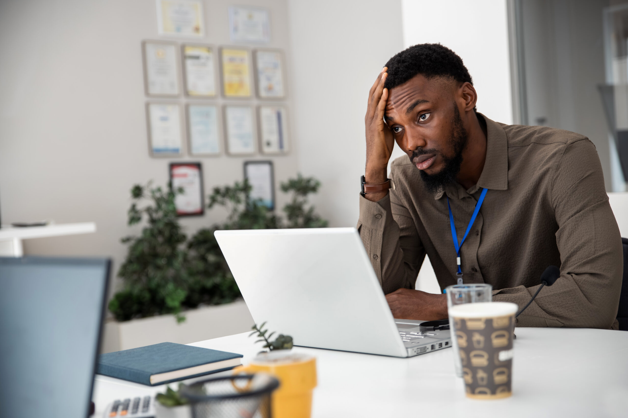 Frustrated black man at his workplace, sitting at desk with laptop