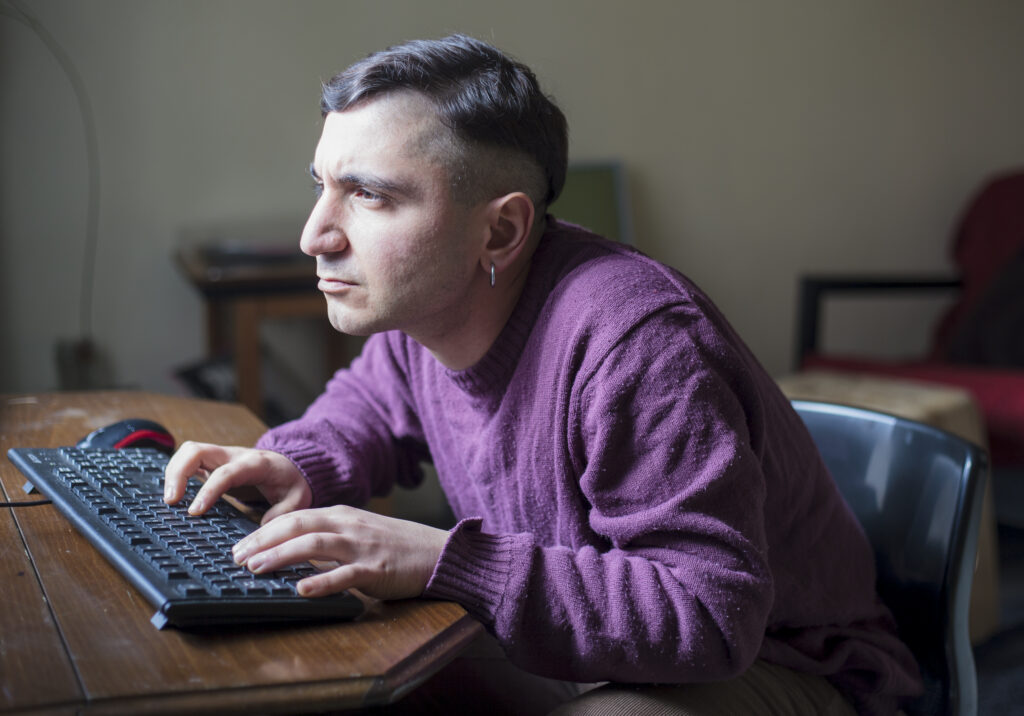 A man sitting at a desk typing, leaned in to better see the computer screen.